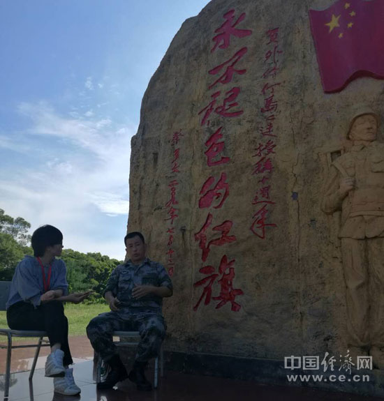 图为杨振英在“永不褪色的红旗”石雕下接受中国经济网记者采访。