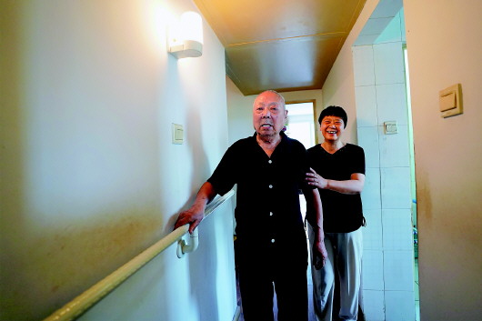 在北京朝阳常营地区民族家园社区,100岁的老人哈云成(左)在家中扶着新安装的沿墙扶手行走(2018年7月10日摄)。新华社记者鞠焕宗摄